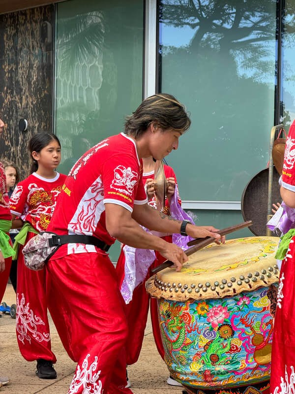 Children playing traditional drums in a festive outdoor setting.
