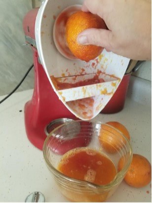 A juicer extracting orange juice into a glass bowl.