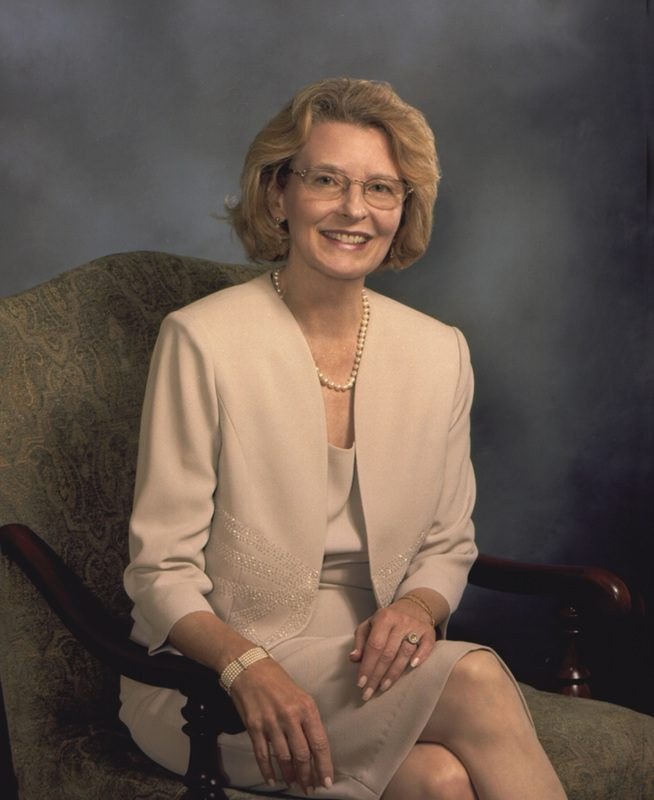A professional woman seated on a chair, smiling at the camera.