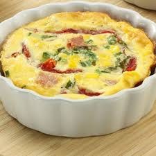 A creamy quiche with spinach and ham in a white ceramic dish.