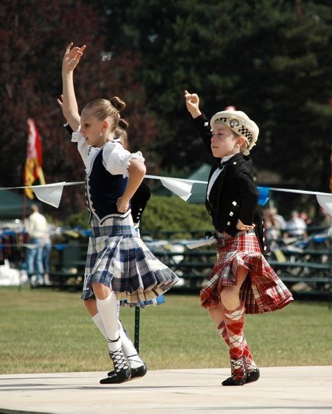 Two children in traditional Scottish attire dancing outdoors.