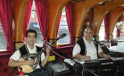Two musicians performing with traditional Greek instruments inside a cozy, curtained room.