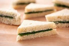 Close-up of triangular cucumber tea sandwiches on wooden board.
