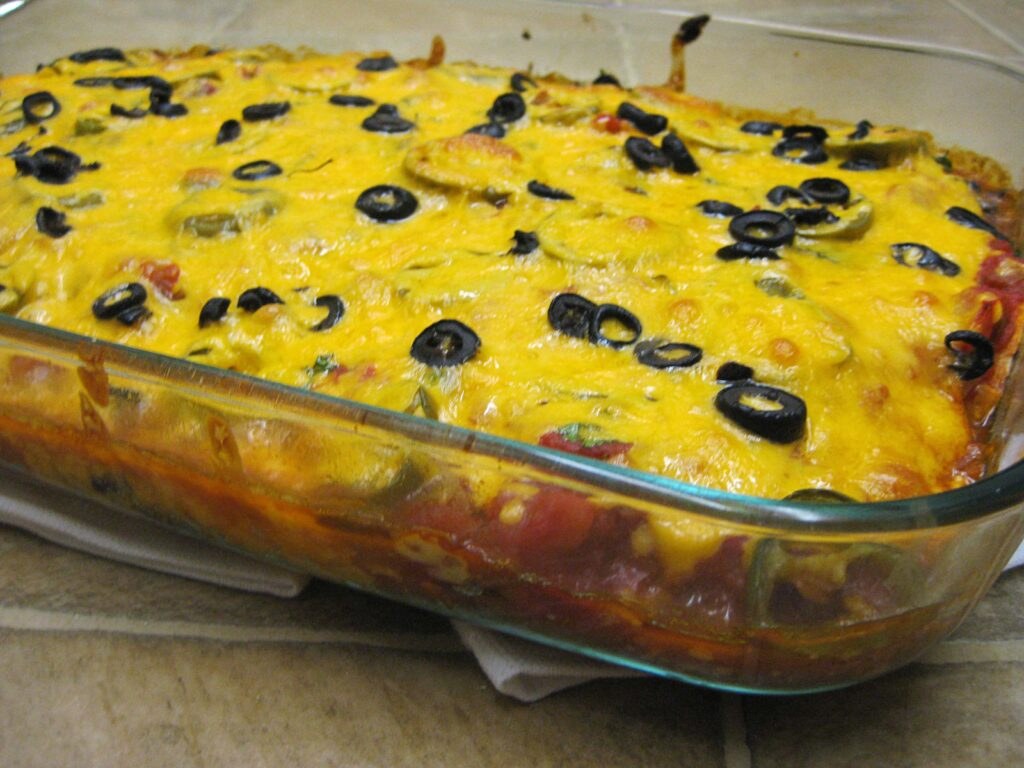 A cheesy baked casserole topped with black olives in a glass dish.