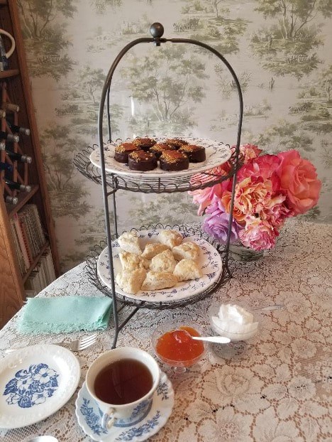 Two-tiered serving tray with pastries and flowers on a table.