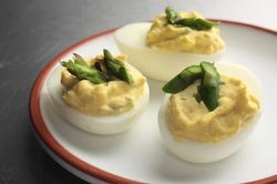 Deviled eggs topped with asparagus spears on a white plate.