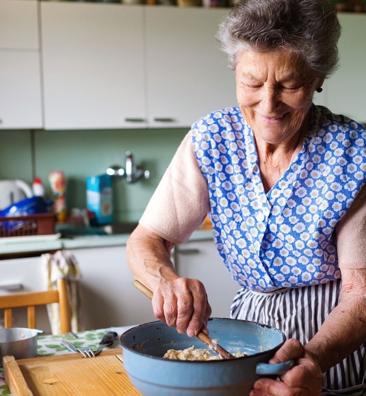 Elderly woman cooking in a cozy kitchen, stirring food in a pan.