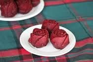 Three red rose-shaped desserts on a white plate.