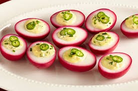 Deviled eggs with a twist, featuring beet-colored shells and green chili toppings.