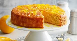 A moist orange cake with a slice removed, displayed on a white cake stand.