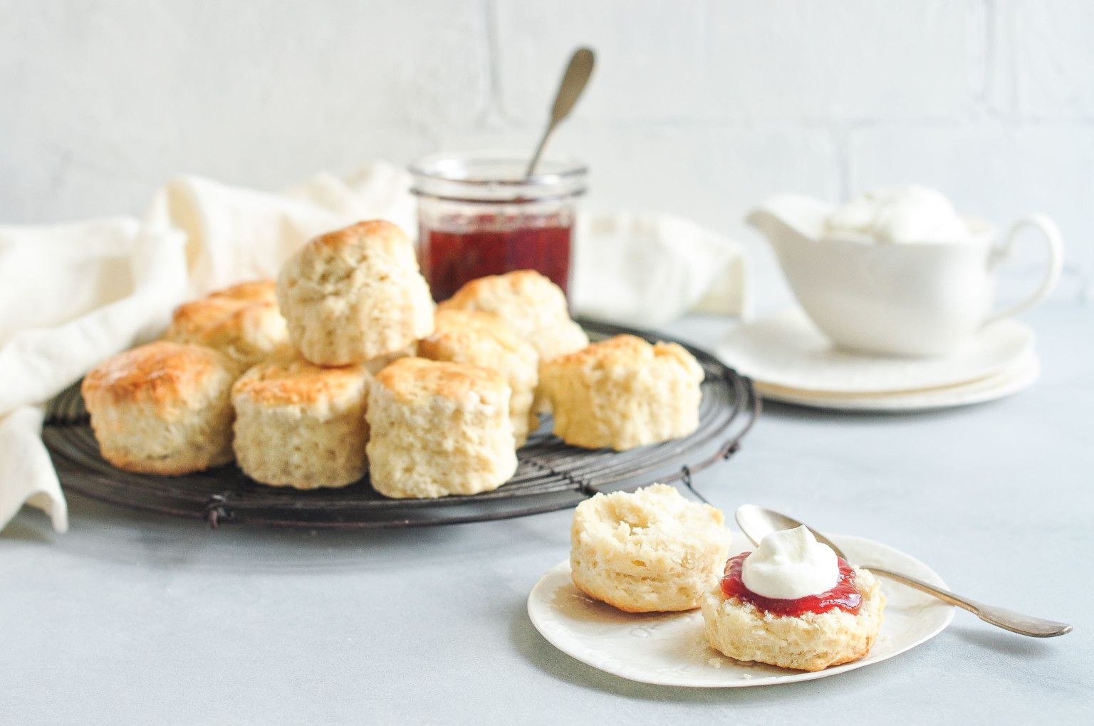 Freshly baked scones with cream and jam on a white table.