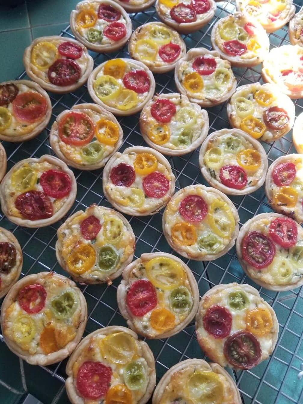Mini quiches topped with colorful cherry tomatoes arranged on a tray.