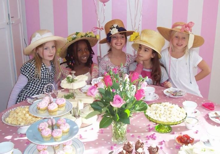 Group of women enjoying a tea party with floral hats and cupcakes.