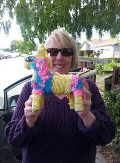Woman holding a colorful piñata shaped like a donkey.