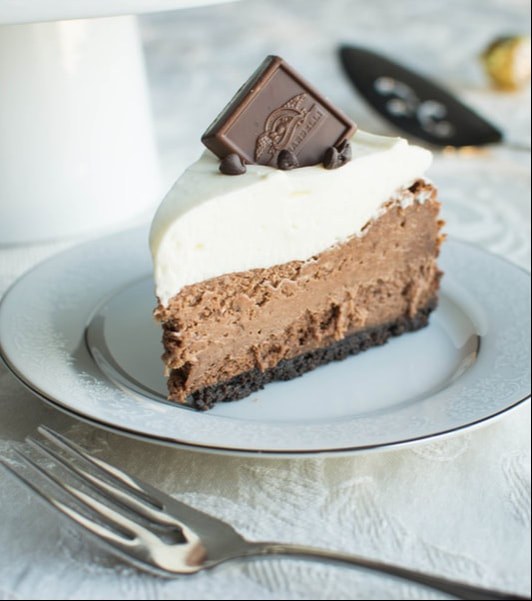 A slice of chocolate mousse cake topped with cream and a chocolate square.