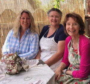 Three women smiling at a table with flowers indoors.