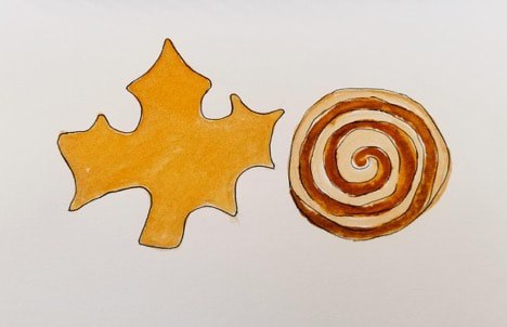 Autumn leaf-shaped cookie and cinnamon swirl pastry on white background.
