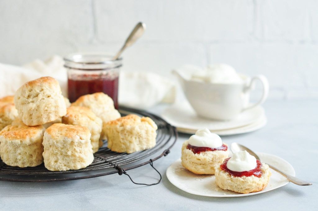 Freshly baked scones with cream and jam on a cooling rack and plate.