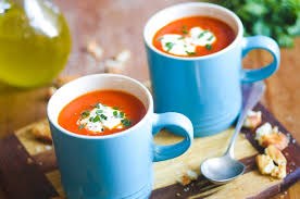 Two blue mugs filled with creamy tomato soup garnished with herbs.