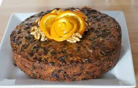 A round fruitcake decorated with an orange peel rose and walnuts on top.