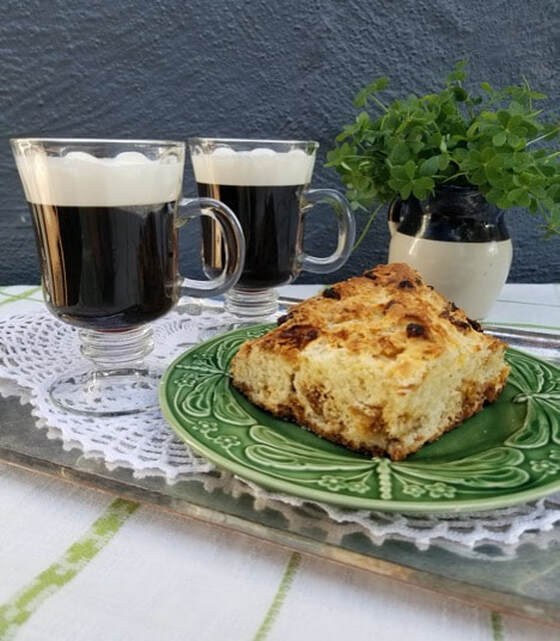 Two mugs of coffee with a slice of crumb cake on a green plate.
