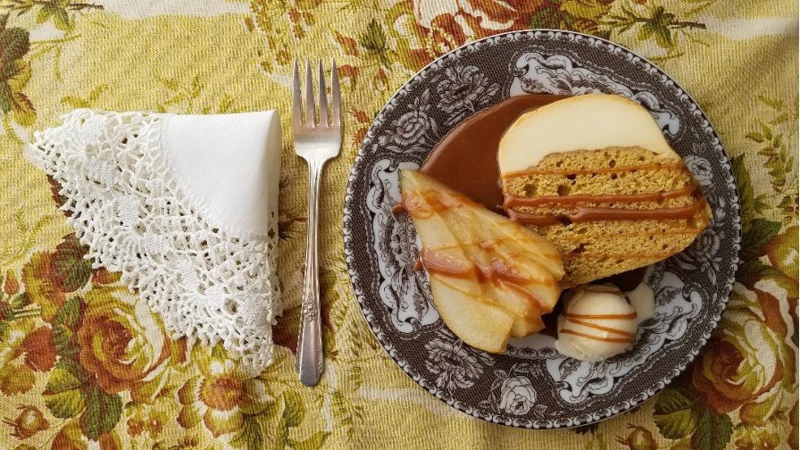 A plate with cake, pear slices, and macarons on a vintage table setting.