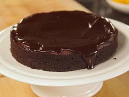 Rich chocolate cake with glossy ganache on a white stand.