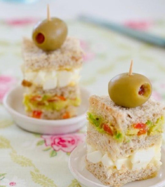Stacked savory appetizer topped with an olive on a floral plate.