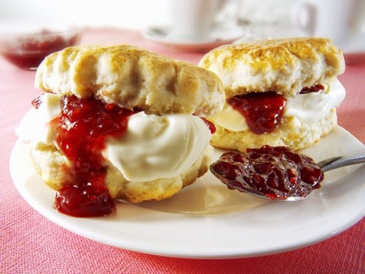Scones filled with clotted cream and strawberry jam on a plate.