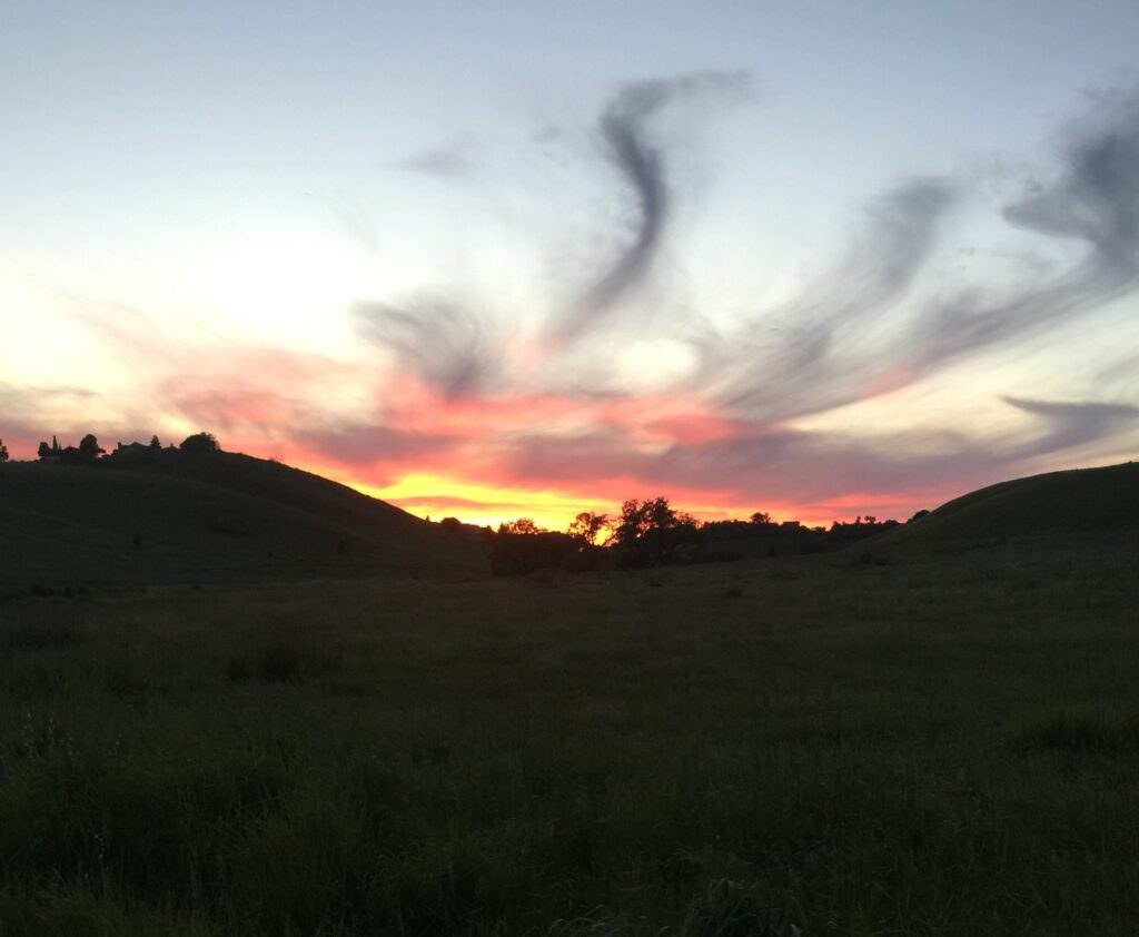 Sunset with colorful clouds over a grassy hill landscape.