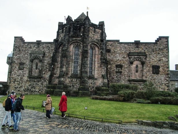 Two people walking near a historic stone building with Gothic architecture.