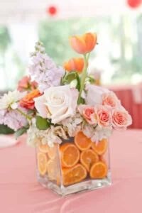 A vibrant floral arrangement with orange slices in a glass vase.
