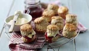 Freshly baked scones with clotted cream and jam on a wire rack.