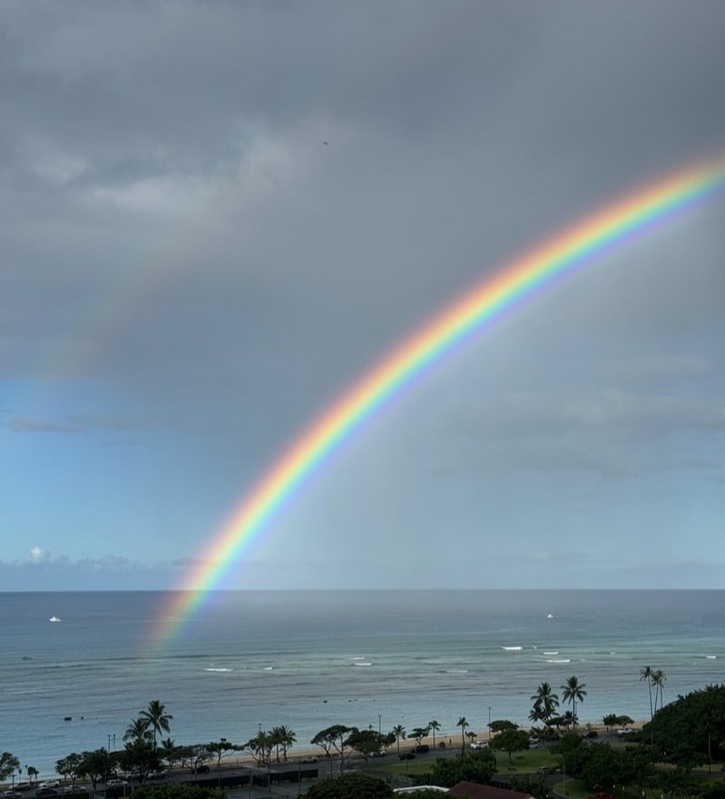 A vibrant rainbow stretches over the ocean under a cloudy sky.