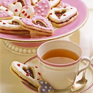Tea cup with heart-shaped cookies on a pink plate.