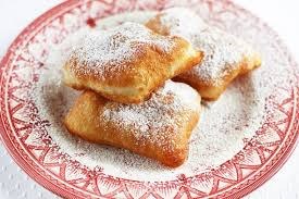 Three beignets dusted with powdered sugar on a decorative plate.