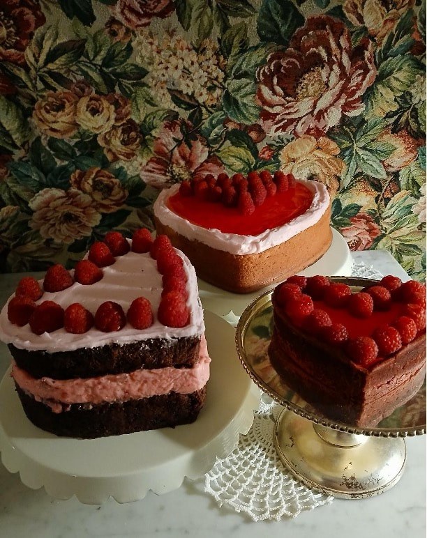 Three heart-shaped cakes decorated with strawberries on a floral tablecloth.