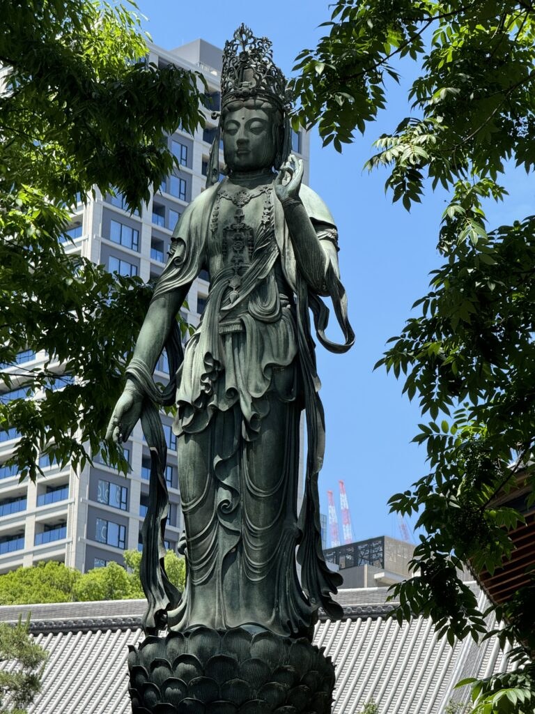 A tall, ornate statue of a serene figure surrounded by greenery in an urban setting.