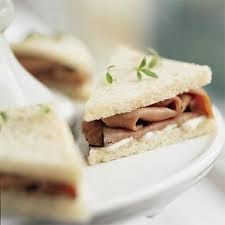 Close-up of a sandwich with meat and herbs on white bread.