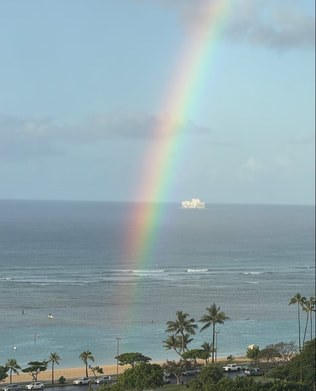 A vibrant rainbow arches over the ocean with a ship on the horizon.