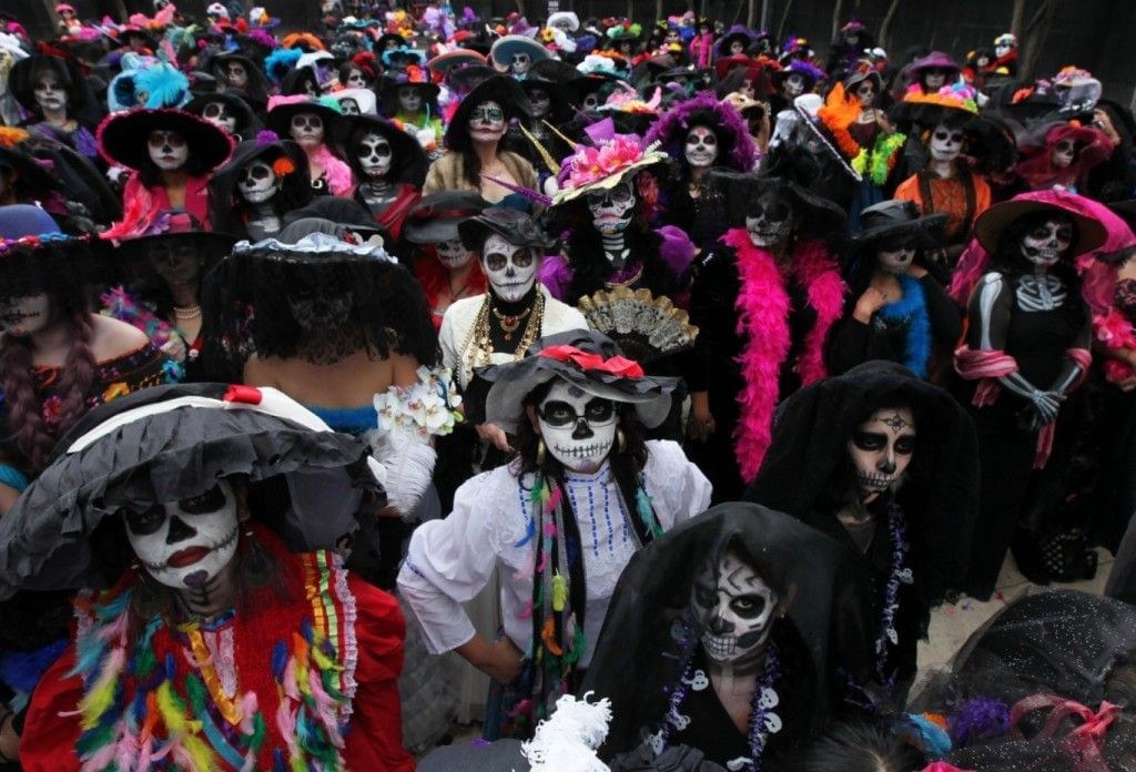 Crowd dressed in colorful, elaborate Day of the Dead costumes and face paint.