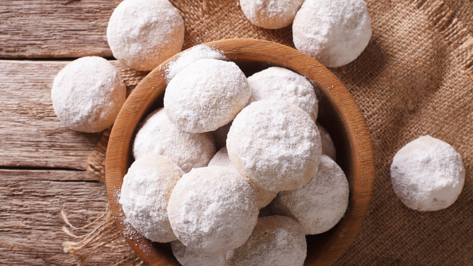 Powdered sugar-coated cookies arranged on a wooden plate.