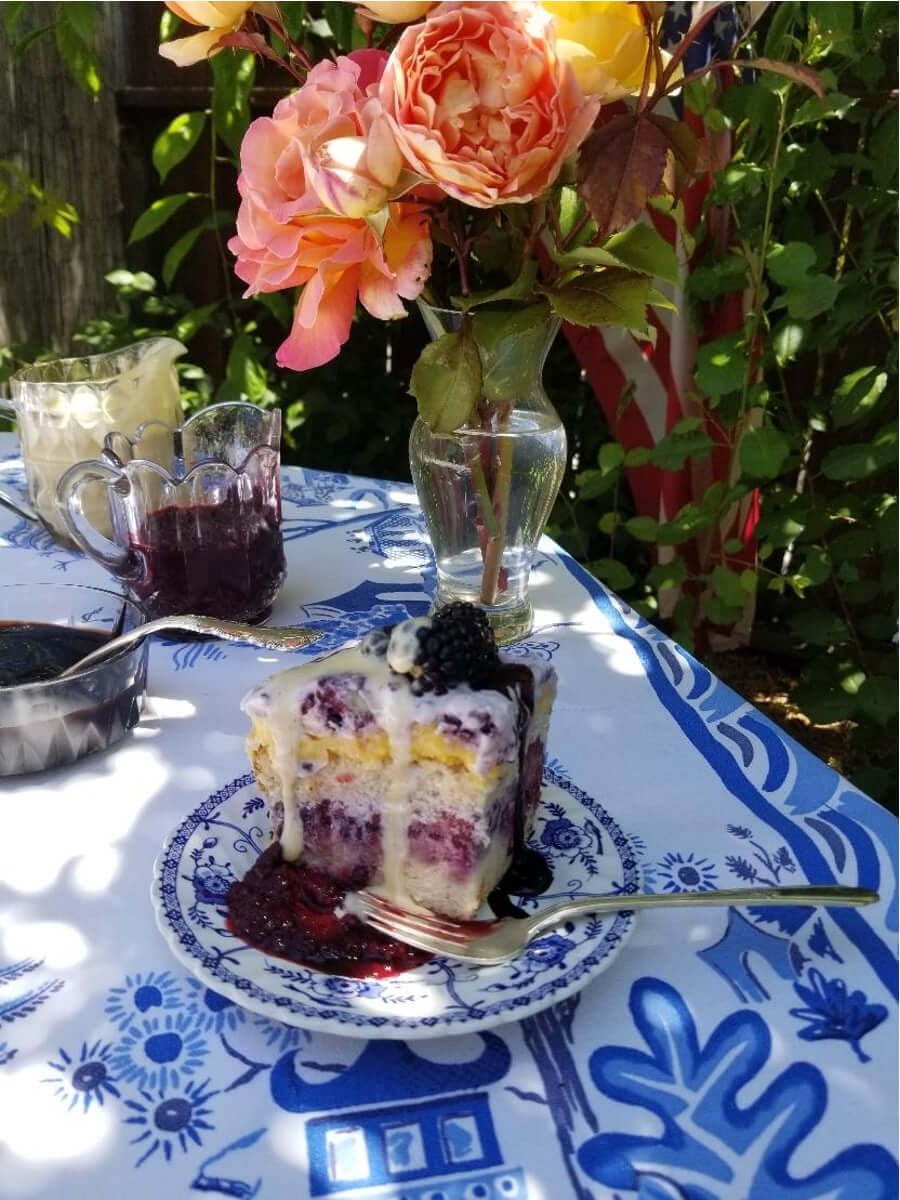 A slice of blueberry cake with cream on a floral plate outdoors.