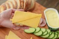 Hand holding sandwich with sliced cheese, cucumbers, and bread.