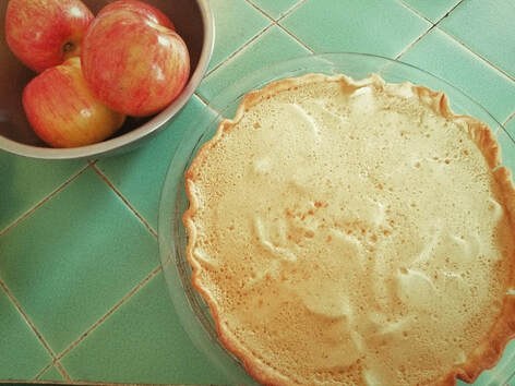 Freshly baked pie with a bowl of apples on the side.