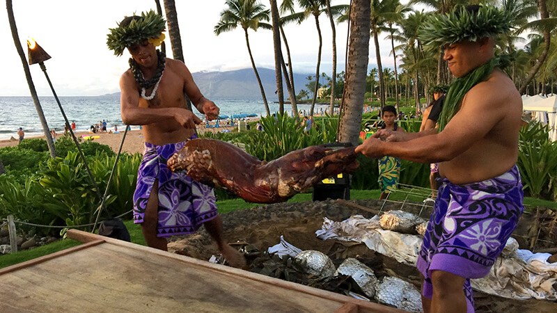 Two men roasting a whole pig outdoors near the beach.