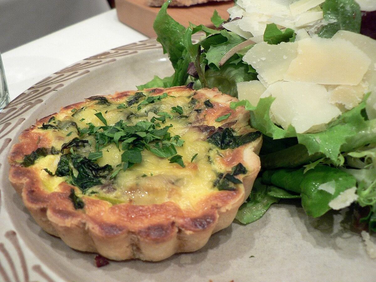 A savory quiche with greens on a plate, served with a side salad.
