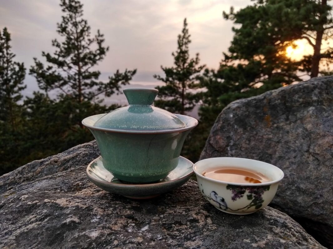Tea set on a rock with a forest and sunset background.