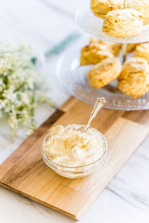 Whipped butter in a glass bowl with freshly baked biscuits on a wooden board.