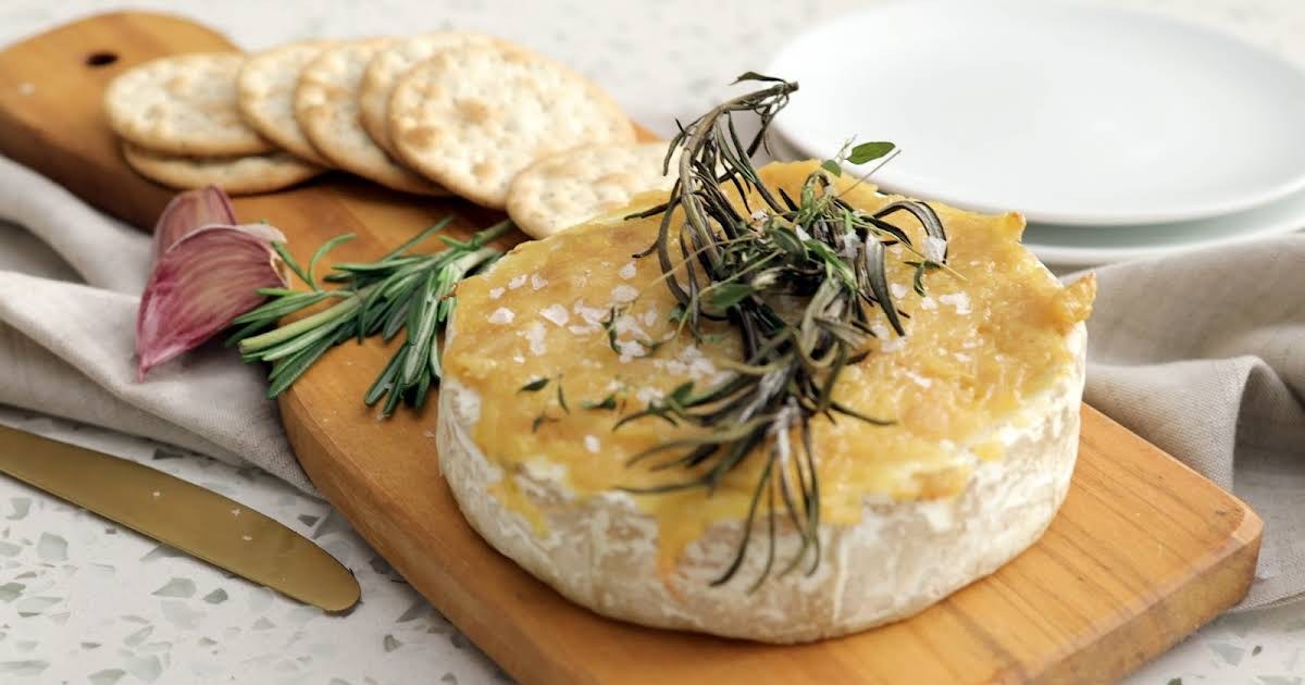 Round cheese topped with rosemary and honey on a wooden board.
